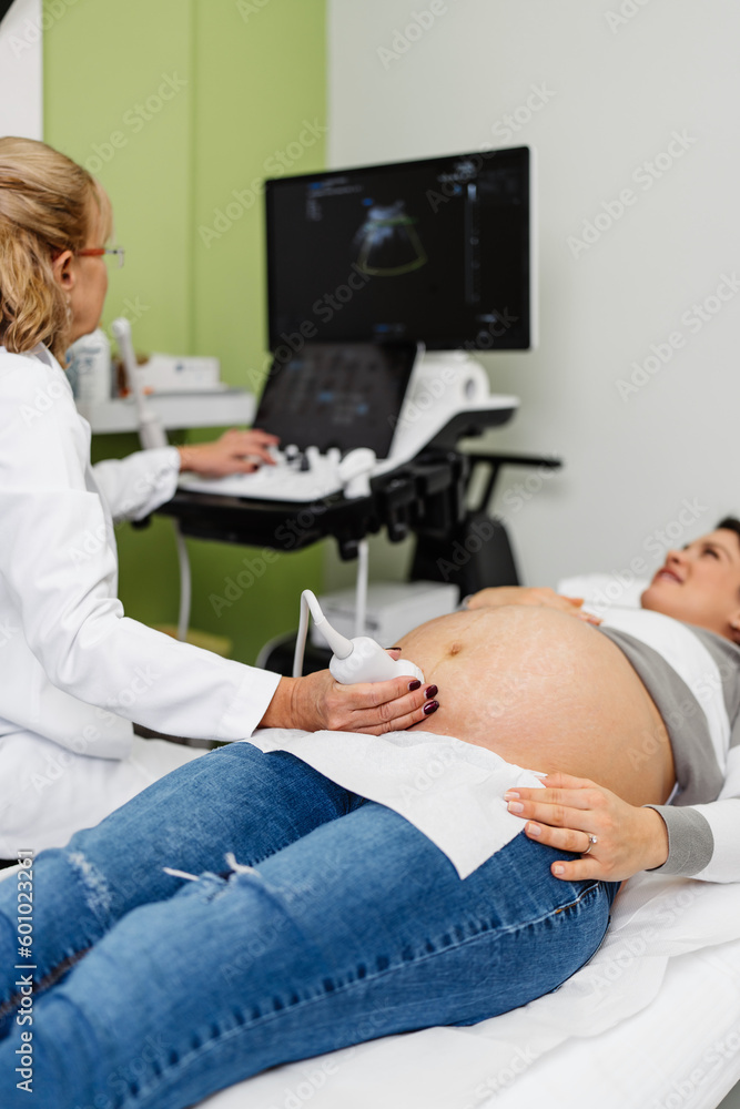Female doctor doing ultrasound scan for a beautiful pregnant woman. Side view. Modern pregnancy and healthcare concept. Female doctor doing ultrasound scan for a beautiful pregnant woman. Side view. Modern pregnancy and healthcare concept.