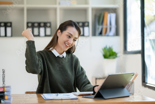 Asian businesswoman raising her hand with a happy expression to receive an email informing her about her annual bonus. concept of success.