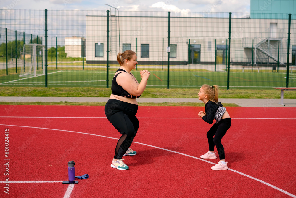 Obraz premium Mother and daughter play sports together in the open area of the stadium. The girl supports her mom by keeping her company in fitness classes