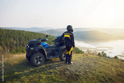  man with helmet standing near quad bike in the mountains and enjoying beautiful view of nature at sunset. photo