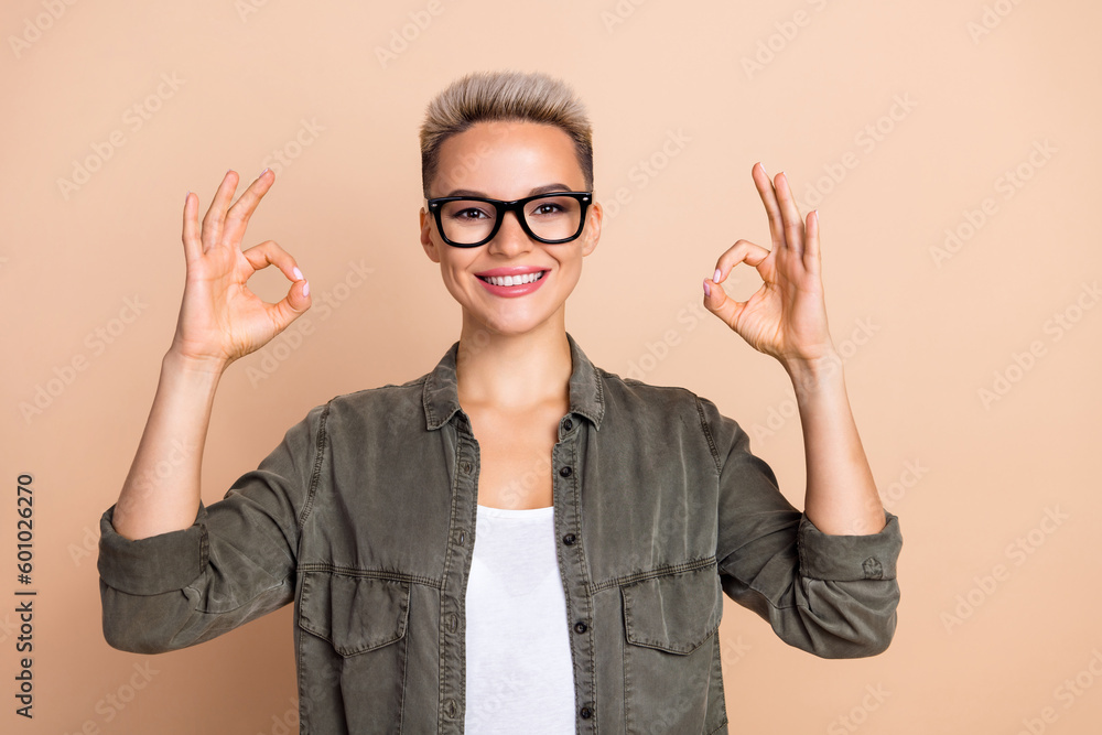 Portrait of friendly cheerful agent girl toothy smile arms fingers demonstrate okey symbol isolated on beige color background Portrait of friendly cheerful agent girl toothy smile arms fingers demonstrate okey symbol isolated on beige color background