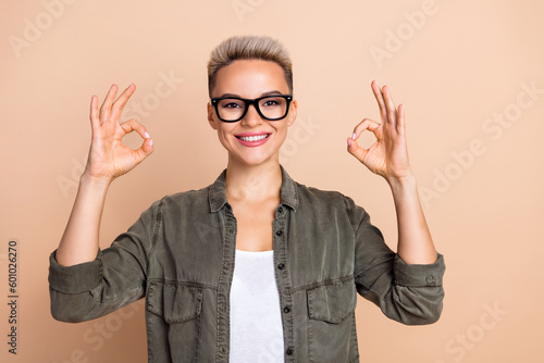 Portrait of friendly cheerful agent girl toothy smile arms fingers demonstrate okey symbol isolated on beige color background