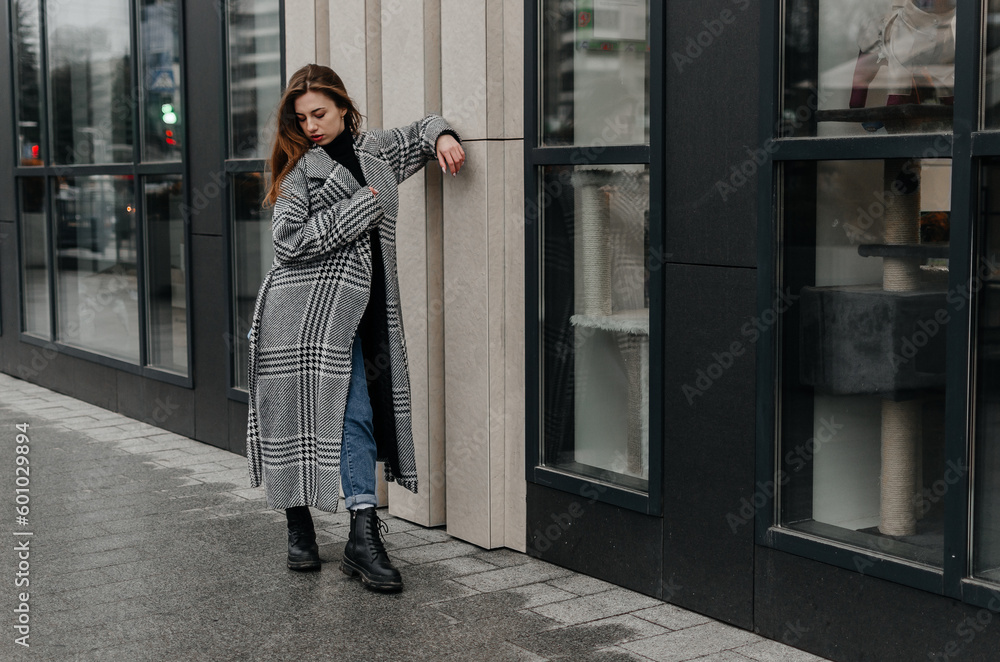 A woman is standing on the sidewalk in front of a house in a gray coat