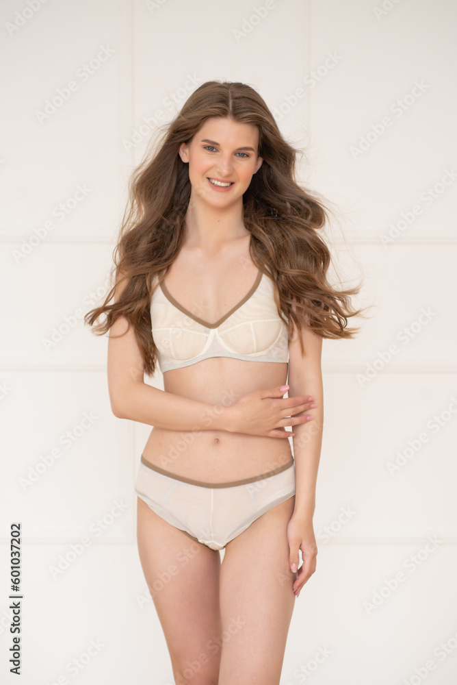 Confident beautiful young woman posing on white background at home in comfortable underwear smiling and looking away. Confident beautiful young woman posing on white background at home in comfortable underwear smiling and looking away.