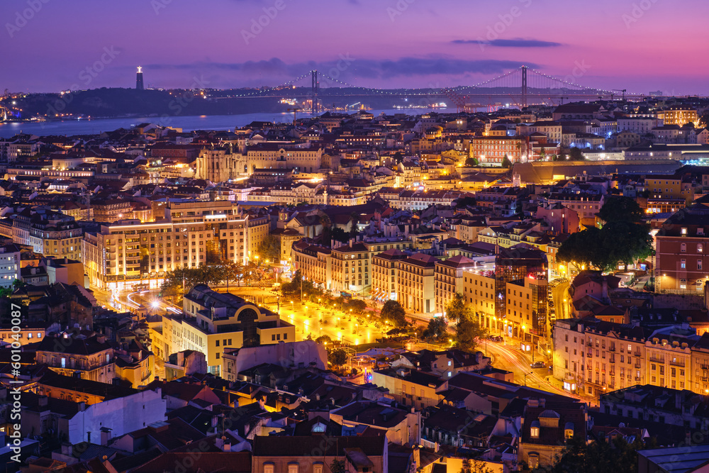 Night view of Lisbon famous view from Miradouro da Senhora do Monte tourist viewpoint of Alfama and Mauraria old city districts, 25th of April Bridge in the evening twilight. Lisbon, Portugal