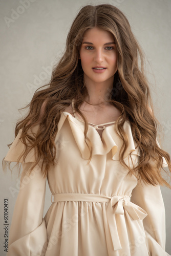 Beautiful young smiling woman portrait with wavy hair, dressed in a beige dress posing in the interior 