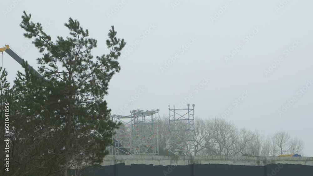 Intensive work on the construction site located near the coast of the sea, large mobile crane moving, overcast day with fog, distant wide shot Intensive work on the construction site located near the coast of the sea, large mobile crane moving, overcast day with fog, distant wide shot