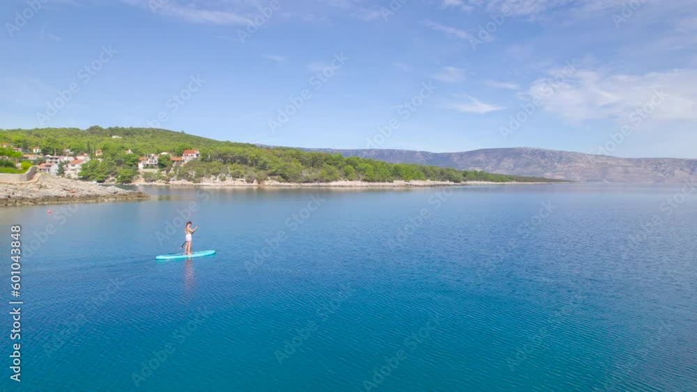 AERIAL: Scenic coast and blue sea water surrounding pretty lady and a dog on SUP. She is on active holidays at a peaceful tourist and travel destination with gorgeous empty beaches during off-season. AERIAL: Scenic coast and blue sea water surrounding pretty lady and a dog on SUP. She is on active holidays at a peaceful tourist and travel destination with gorgeous empty beaches during off-season.