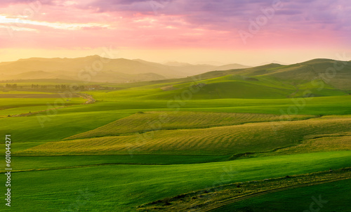 beautiful green valley with green fields with green spring grass with nive hills and mountains and scrnic colorful cloudy sunset on background of landscape © Yaroslav