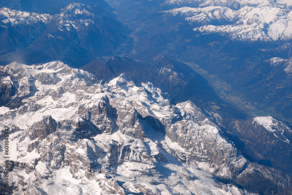 Stunning aerial view through porthole of plane to the snowy and sunny Alps. Airplane. Travelling by air.