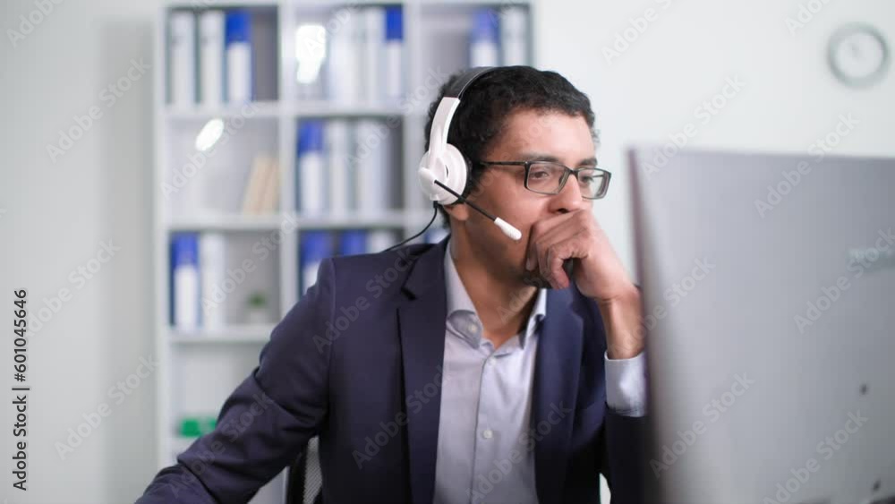 black man in glasses works in a call center consults client using a headset on video call while sitting at a computer in office black man in glasses works in a call center consults client using a headset on video call while sitting at a computer in office