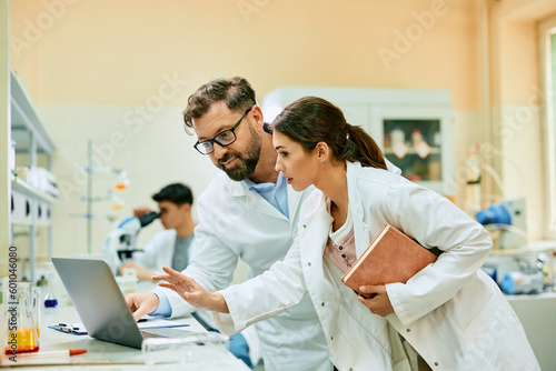 Young scientist and her colleague analyzing medical research data on computer while working in lab.