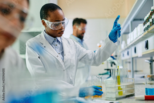 Black biotechnologist analyzing chemical samples during scientific research in lab.