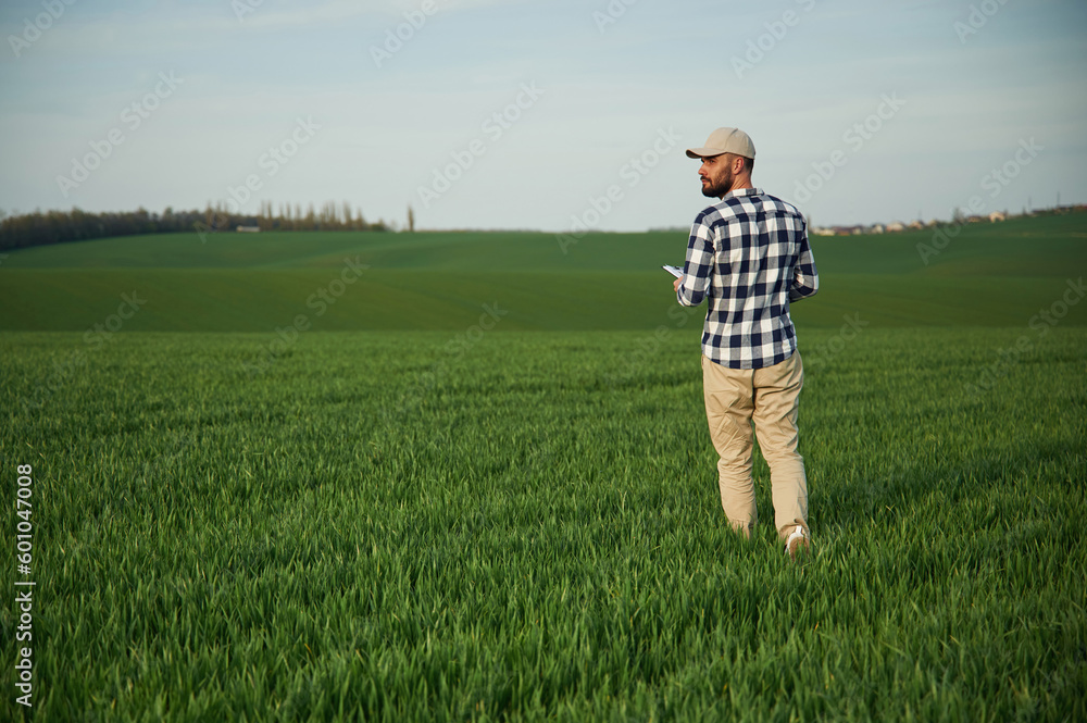 Walking, holding notepad. Handsome young man is on agricultural field Walking, holding notepad. Handsome young man is on agricultural field