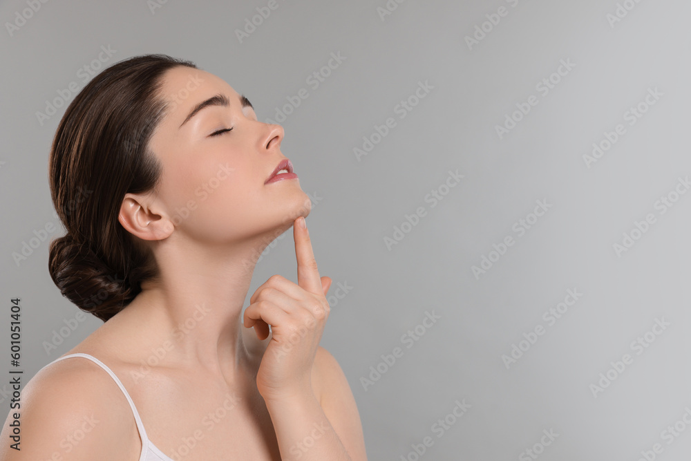 Young woman massaging her face on grey background. Space for text Young woman massaging her face on grey background. Space for text