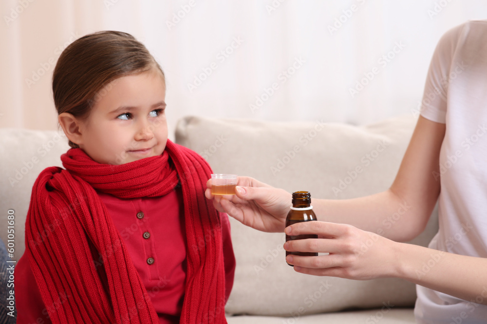 Mother giving cough syrup to her daughter on sofa indoors Mother giving cough syrup to her daughter on sofa indoors