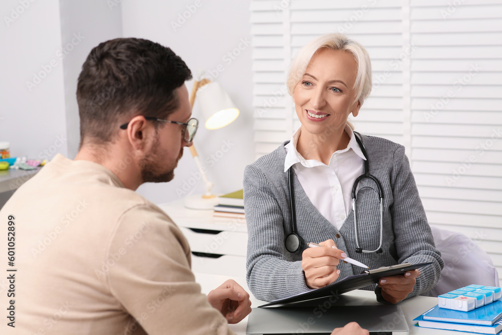 Doctor with pen and clipboard consulting patient at table in clinic