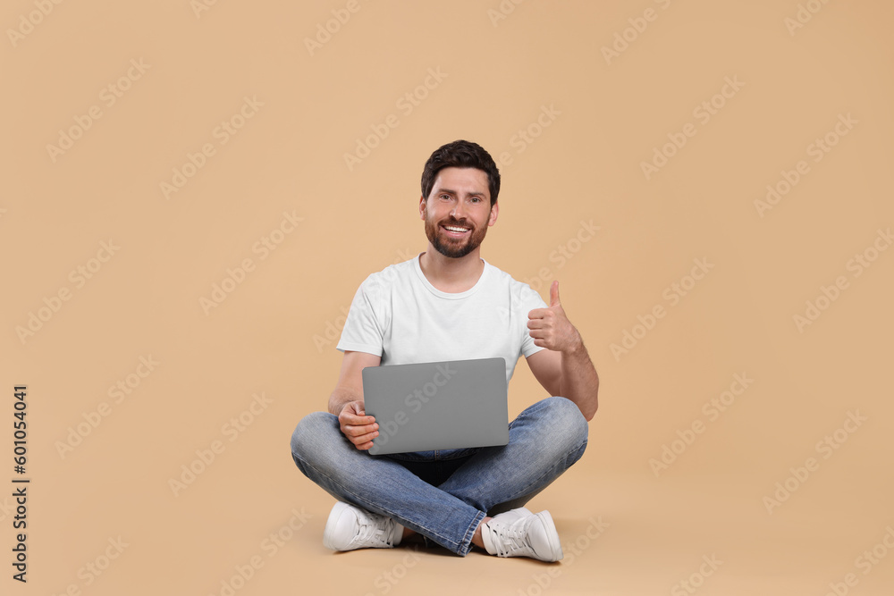Happy man with laptop showing thumb up on beige background Happy man with laptop showing thumb up on beige background