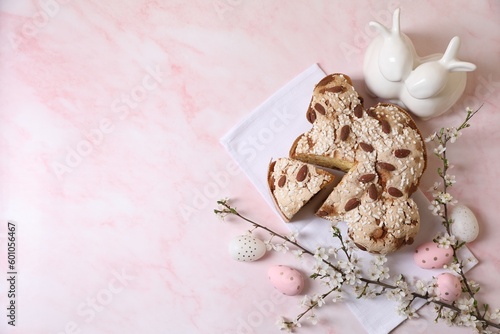 Delicious Italian Easter dove cake (traditional Colomba di Pasqua), painted eggs, figure of rabbits and branches with flowers on pink marble table, flat lay. Space for text