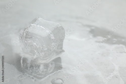 One clear ice cube on light grey table, closeup. Space for text