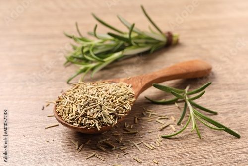 Spoon with dry rosemary and fresh twigs on wooden table, closeup