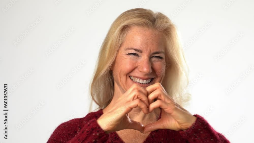 Cheerful happy senior mature woman shows heart gesture with hands showing love, smiling isolated on solid white background Cheerful happy senior mature woman shows heart gesture with hands showing love, smiling isolated on solid white background