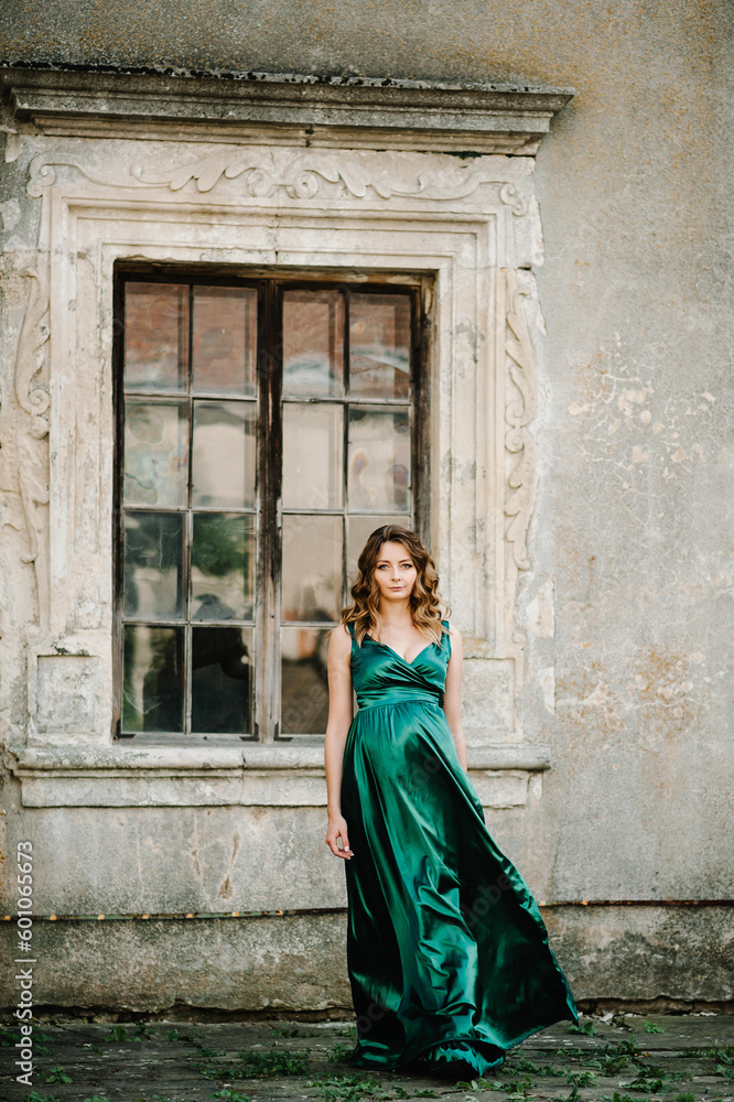 Pregnant woman wearing long green dress walking on the street near old window. New life concept. Waiting baby.