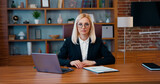 Portrait of lovely concentrated adult blond businesswoman in formal wear which sitting in front of camera in modern office