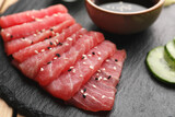 Tasty sashimi (pieces of fresh raw tuna with sesame seeds) on black board, closeup