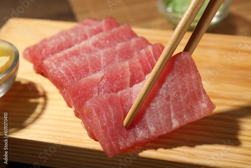 Taking tasty sashimi (piece of fresh raw tuna) from wooden board, closeup