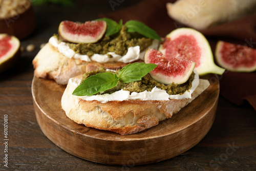 Tasty bruschettas with cream cheese, pesto sauce, figs and fresh basil served on wooden table, closeup