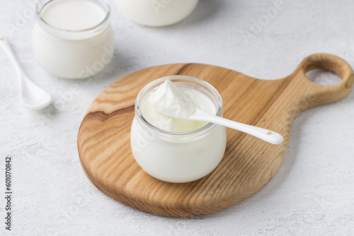 Natural homemade yogurt in a glass jar on a wooden board on a light gray background