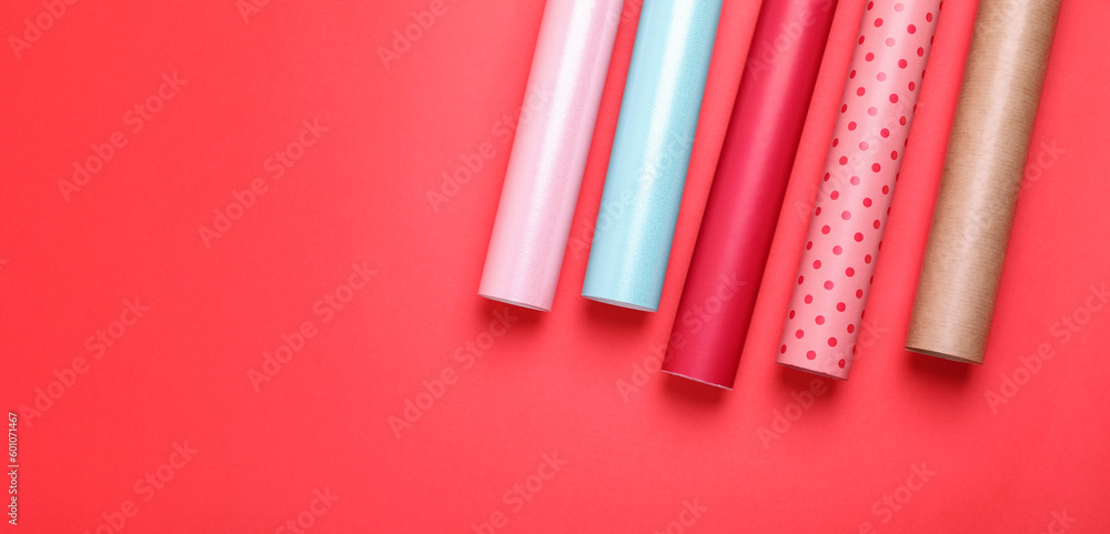 Rolls of colorful wrapping papers on red background, flat lay. Space for text