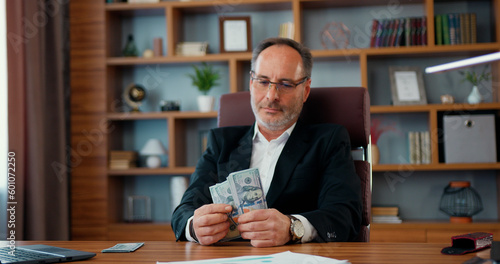 Handsome confident experienced adult bearded businessman counting dollars banknotes cash in his modern office,business and success concept