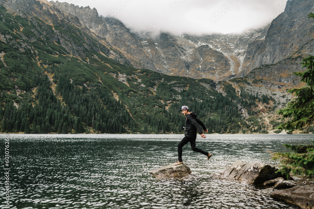 A Man jumping on the stony shore near the lake in the mountains. Boy against the backdrop of a mountain landscape. Scenic mountain view. A Man jumping on the stony shore near the lake in the mountains. Boy against the backdrop of a mountain landscape. Scenic mountain view.