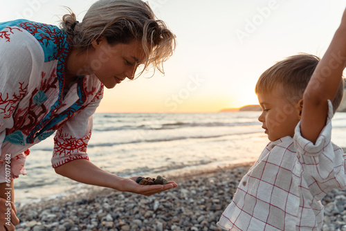 Mother and her cute little son collecting pebbles on shingle beach