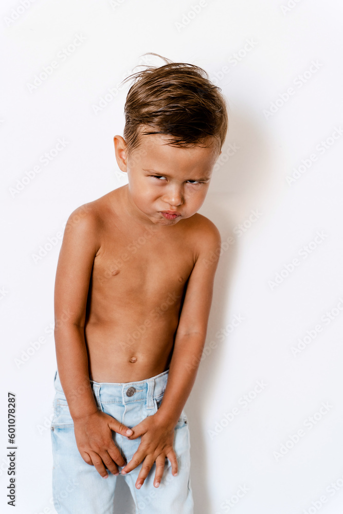 Cute little boy wearing blue jeans posing against white background with silly facial expression Cute little boy wearing blue jeans posing against white background with silly facial expression
