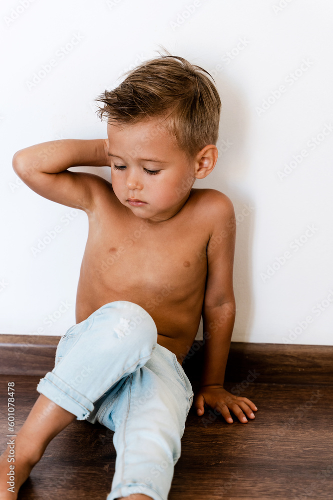 Cute little boy wearing blue jeans posing against white wall like fashion model Cute little boy wearing blue jeans posing against white wall like fashion model