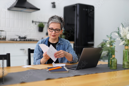 Serious mature woman at a table in a home interior looks through mail and bank accounts.