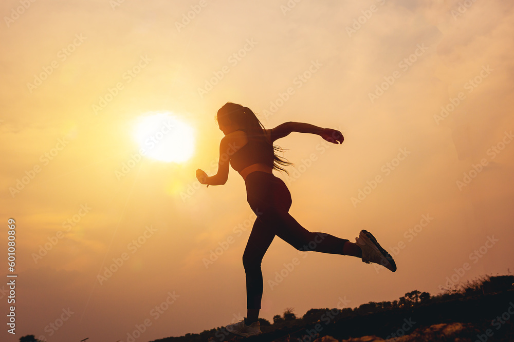 Silhouette of young woman running sprinting on road. Fit runner fitness runner during outdoor workout with sunset background. Silhouette of young woman running sprinting on road. Fit runner fitness runner during outdoor workout with sunset background.