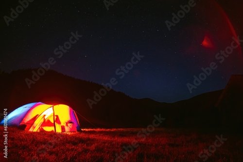 The tourist tent is illuminated by light. Starry sky. Tourism and active recreation. Overnight, camping in the Carpathian mountains, Ukraine. Copy space.