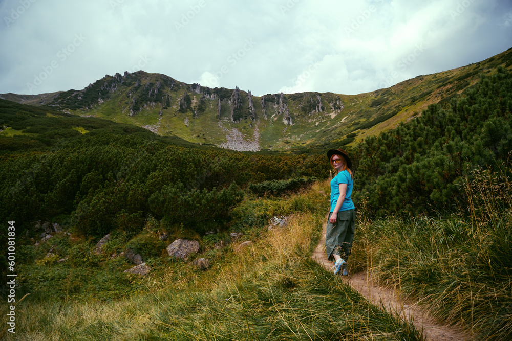 The back view of a girl hiker hiking to the top of Spytsi mountain, Carpathians, Ukraine. He has a long stick in his hands. Travel and active recreation. Copy space