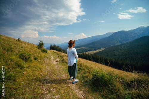 Back view of woman in leather hat standing alone on viewpoint and looking at distance mountain. Sunny summer day. Carpathians mountains Ukraine.