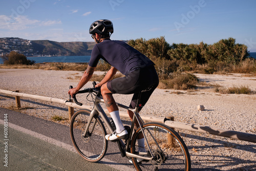 Fototapeta Naklejka Na Ścianę i Meble -  Professional male cyclist riding on bicycle near sea. Spanish cycling holiday. Motivational image. Triathlon concept. Xàbia, Alicante, Spain