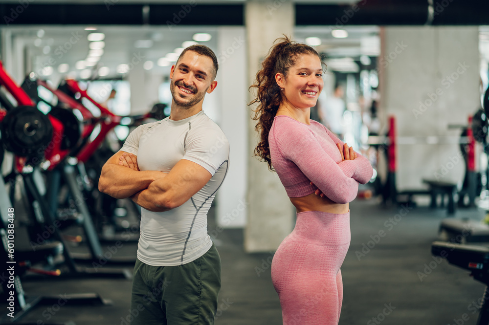 Obraz premium A cheerful confident sporty couple is standing in a gym with arms crossed and smiling at the camera.