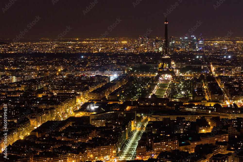 Fototapeta premium Aerial view of Paris at night with a dark Eiffel Tower and La DÃ©fense business district in the background, as seen from the Tour Montparnasse, France