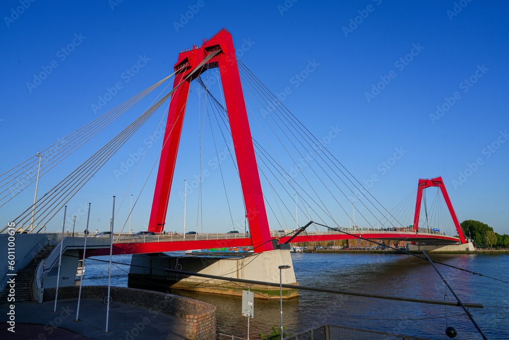 Fototapeta premium View of the Willemsbrug suspension bridge in Rotterdam, crossing the Nieuwe Maas river in the Netherlands - Red steel road bridge with two towers
