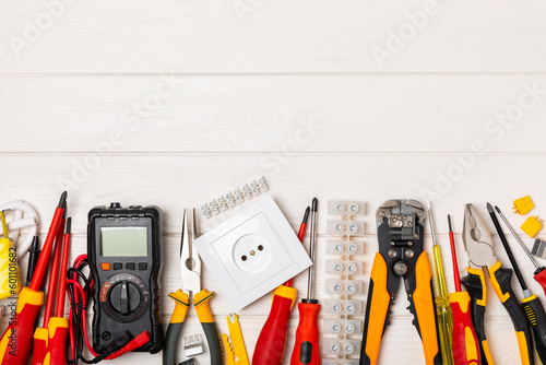 Electrician tools on white wooden background.Multimeter,construction tape,electrical tape, screwdrivers,pliers,an automatic insulation stripper, socket and LED lamp.Flatley.electrician concept.