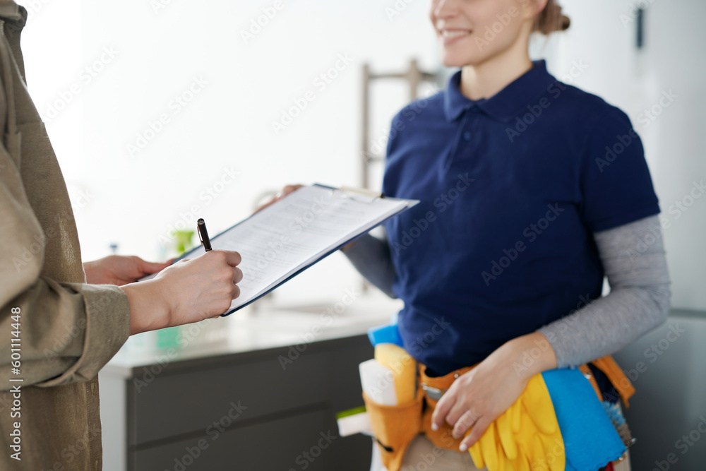 Close-up of housewife signing a contract with cleaning service worker to hire professional to do housework - obrazy, fototapety, plakaty 