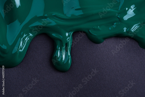 Dark green liquid drops of paint color flow down on black paper. Abstract art. Green paint dripping on the black wall